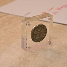 a small glass block with a coin in the center on a counter top next to a piece of paper