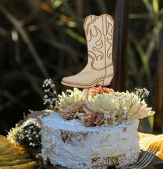 a cake decorated with flowers and a cowboy boot topper sits on a table outdoors