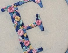 the letter f is made up of flowers and leaves on a white fabric with blue trim