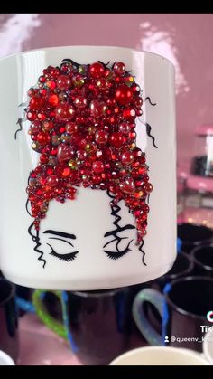 a white mug with red beads and a woman's face on it is hanging from the ceiling