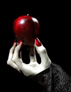 a woman holding an apple up to her face in front of a black background with white hands