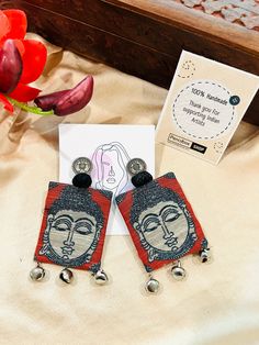 two earrings are sitting on a bed next to a card and red tulips