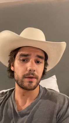 a man wearing a white cowboy hat sitting on top of a bed in front of a gray wall