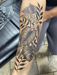 a person with a tattoo on their arm that has leaves and flowers on it,