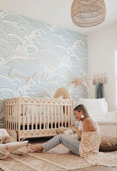 a woman sitting on the floor next to a baby crib