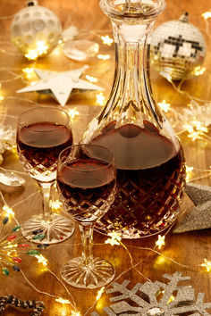 two glasses of wine sit in front of a decanter and snowflakes