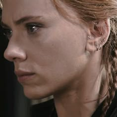 a close up of a person with braid hair and piercings on her ear, looking off to the side