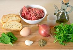 ingredients to make meatloaf on a cutting board including bread, onions, garlic and herbs