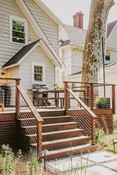 a house with stairs leading up to the front door and back porch area, next to a tree