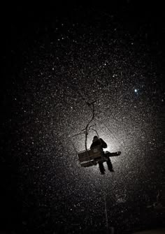 a person on a ski lift in the dark with snow falling off their feet and arms