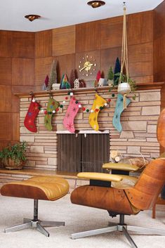 an eames chair and ottoman in front of a fireplace with stockings hanging on the mantle