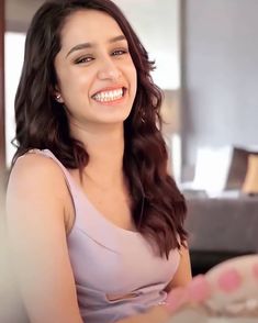 a woman with long brown hair smiling and wearing a purple dress in front of a couch