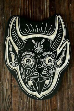 a black and white mask with horns on it's face is hanging on a wooden wall