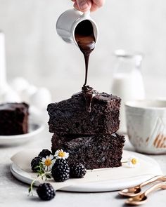 someone pouring chocolate sauce on top of some brownies with berries and raspberries