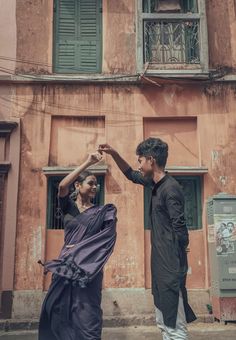 a man and woman dancing in front of an old building with shutters on the windows