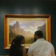 a man and woman sitting in front of a painting on display at a museum looking at each other