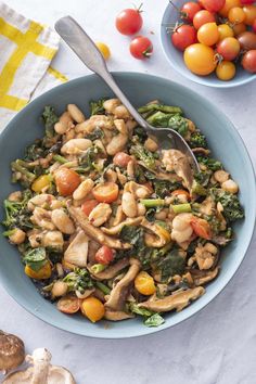 a blue bowl filled with mushrooms, spinach and cherry tomatoes next to other vegetables