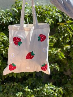 This strawberry tote bag with flowers is fun, lightweight, and is the perfect eco friendly reusable grocery tote bag. The strawberries add beautiful bright color, fun, and a cute aesthetic to go with your outfits. Use you tote bag in place of a purse, to carry your laptop, water bottle or other goodies.  This canvas tote is natural color and is 100% cotton.  Strawberry pattern may differ slightly as they are hand placed. CARE INSTRUCTIONS: Wash inside out on a gentle cycle. Hang dry. Iron inside out. Do not iron directly on top of the design.  Please message us with any questions.  Thank you! Tote Bag Pattern Paint, Flower Tote Bag Painting, Cute Strawberry Print Tote Bag, Cute Spring Tote Bag, Tote Bag Design Ideas Paint, Summer Strawberry Print Bag For Daily Use, Summer Strawberry Print Bags For Daily Use, Cute Reusable Tote Bag