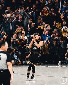 a basketball player is in the middle of a game with his hands up and people are clapping behind him