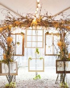 an arrangement of flowers and branches in vases under a white tented area with windows