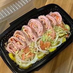 a plastic container filled with meat and veggies on top of a wooden table