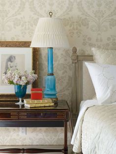 a blue vase sitting on top of a wooden table next to a lamp and bed