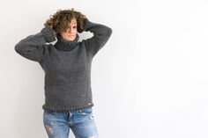 a woman in ripped jeans and a gray sweater is holding her hands on her head