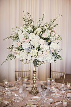 a tall vase filled with white and pink flowers on top of a table covered in silverware