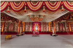 a man sitting on a chair in front of a stage decorated with flowers and garlands