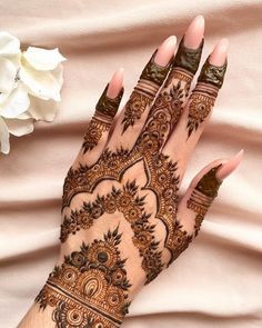 a woman's hand with henna tattoos on it and flowers in the background