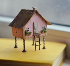 a miniature house on top of a book with a ladder to the roof and windows