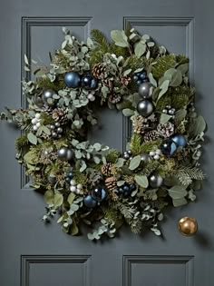 a christmas wreath hanging on the front door with evergreen leaves, berries and pine cones