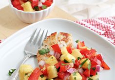 a white plate topped with meat and veggies next to a bowl of fruit