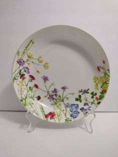 a white plate with flowers painted on the front and sides, sitting on a stand