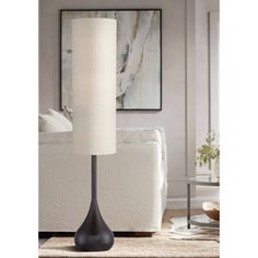 a floor lamp with a white shade on it in a living room next to a couch