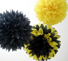 three black, yellow and white paper flowers hanging from the ceiling in front of a wall