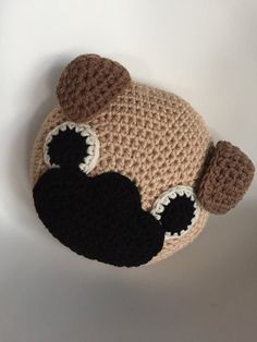 a crocheted teddy bear hat with black eyes and ears is shown against a white background