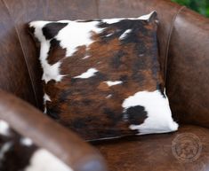 a brown and white cowhide pillow sitting on top of a brown leather chair next to a green wall