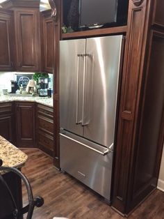 a stainless steel refrigerator in a kitchen with wooden cabinets and granite counter tops, along with a microwave on the wall