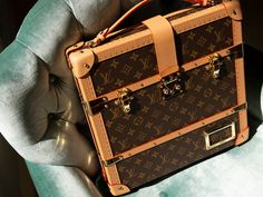 a brown and tan louis vuitton suitcase sitting on top of a blue chair