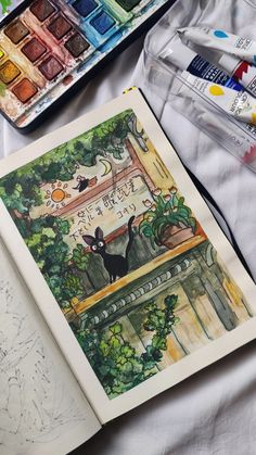 an open book sitting on top of a table next to watercolors and markers