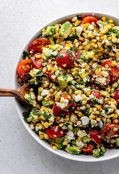 a white bowl filled with corn, tomatoes and cucumber on top of a table