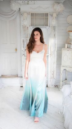 a woman in a white and blue ombreed dress standing next to a bed