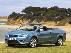 a blue convertible car parked on top of a lush green field next to the ocean