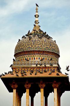 an ornate dome with birds on top and blue sky in the background, surrounded by yellow pillars