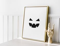 a wooden hand is next to a framed halloween poster on a white wall with a gold frame