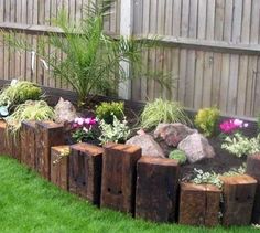 a garden with rocks and flowers in the grass next to a wooden fenced area