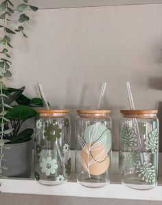 three glass jars with straws and plants in them sitting on a shelf next to a potted plant