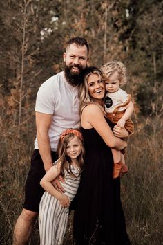 a man, woman and two children are posing for a family photo in the woods