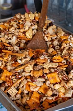 a metal pan filled with chex mix and a wooden spoon sticking out of it